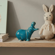 Decorative shelf with a blue hippo figurine, beige rabbit toy, and books against a neutral wall.